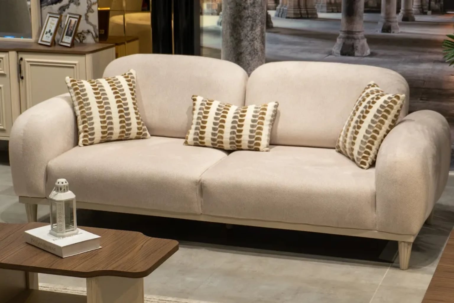Zarif krem rengi kumaş koltuk takımının bulunduğu, doğal ahşap sehpalı ve yumuşak ışıklı modern bir salon.